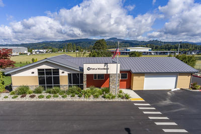 A picture of the Port of Woodland Office building with a flag pole and a vacant property in the background.